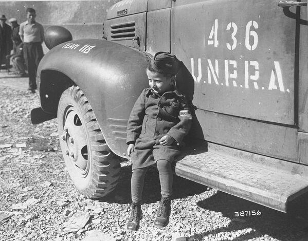 جوزيف شليفشتاين، أربعة أعوام، أحد الناجين من لمعسكر التركيز النازي بوتشينوالد، يسند على سيارة تابعة لمنظمة إدارة الأمم المتحدة للإغاثة والتأهيل (أونرا) بعد تحرير المخيم بقليل، عام 1945 - سبوتنيك عربي