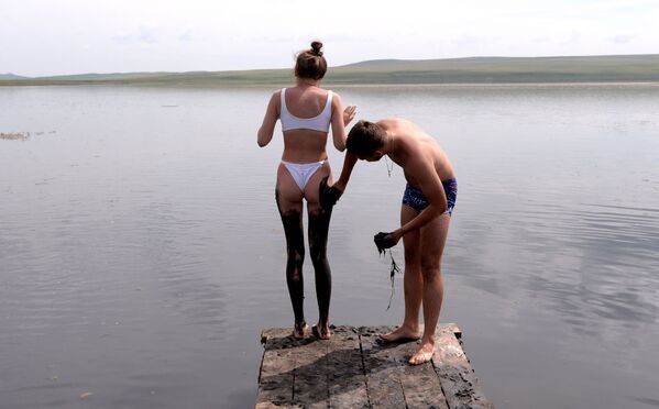 رجل يضع طين الكبريتيد على جسم المرأة من بحيرة طوس في منطقة شيرينسكي بجمهورية خاكاسيا الروسية، 13 يوليو 2020 - سبوتنيك عربي