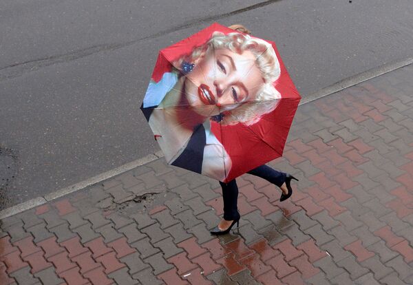 امرأة تحمل مظلة مرسوم عليها الفنانة ميرلين مونرو وتسير في الشارع أثناء عاصفة ممطرة في كراسنويارسك الروسية، 10 يوليو 2020 - سبوتنيك عربي