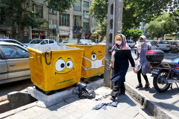 امرأة تسير بجوار سلة قمامة مرسوم عليها كمامة، في إطار حملة لنشر الوعي حول جائحة كورونا، في حي جنوبي بالعاصمة الإيرانية طهران في 18 يوليو 2020. - سبوتنيك عربي