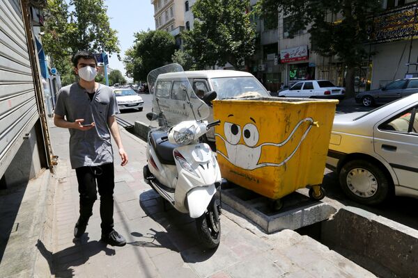 رجل يسير بجوار سلة قمامة مرسوم عليها كمامة، في إطار حملة لنشر الوعي حول جائحة كورونا، في حي جنوبي بالعاصمة الإيرانية طهران في 18 يوليو 2020. - سبوتنيك عربي