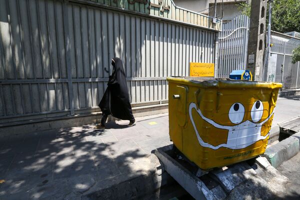 امرأة تسير بجوار سلة قمامة مرسوم عليها كمامة، في إطار حملة لنشر الوعي حول جائحة كورونا، في حي جنوبي بالعاصمة الإيرانية طهران في 18 يوليو 2020. - سبوتنيك عربي