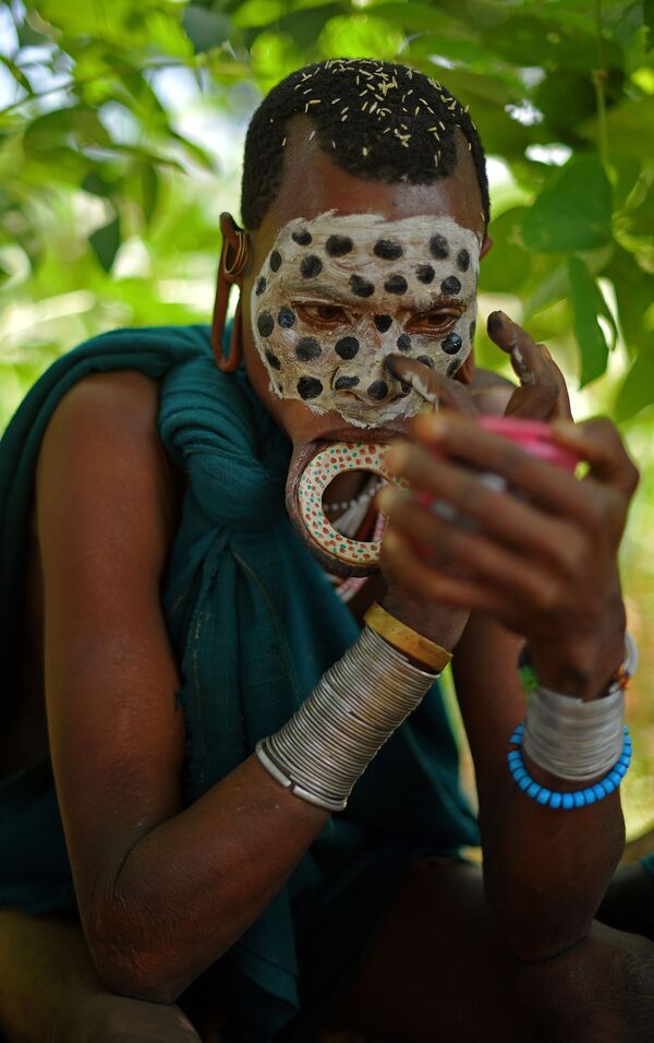 امرأة من قبيلة سوري لديها قرص شفاه وتقوم بتزيين وجهها بألوان قبيلتها التقليدية، في منطقة وادي أومو جنوب إثيوبيا - سبوتنيك عربي