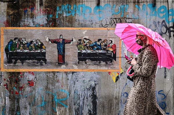امرأة ترتدي كمامة تمر أمام لوحة جدارية جديدة لفنان الشارع الإيطالي TvBoy، بعنوان عشاء لستة أشخاص، مستوحاة من العشاء الأخير للفنان الإيطالي ليوناردو دا فينشي في جنوب مديمة ملاينو، إيطاليا 27 أكتوبر 2020 - سبوتنيك عربي