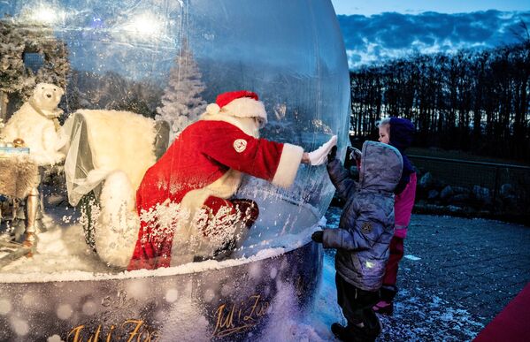 شخص يرتدي زي بابا نويل يلتقي بأطفال أثناء جلوسه في فقاعة سانتا كلوز أثناء افتتاح موسم الكريسماس في حديقة حيوانات ألبورغ وسط تفشي مرض فيروس كورونا (كوفيد-19)، في آلبورغ، الدنمارك، 13 نوفمبر 2020. - سبوتنيك عربي