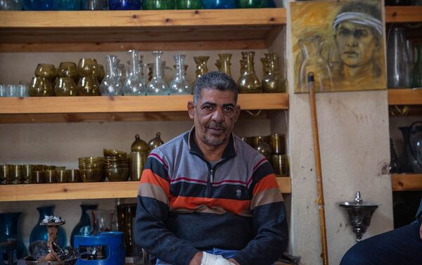 خالد علي صاحب ورشة صناعة الزجاج اليدوي، يجلس أمام بعض منتجاته - سبوتنيك عربي