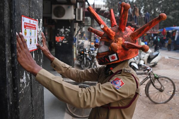 متطوع في الدفاع المدني يرتدي خوذة مستوحاة من فيروس كورونا، يلصق لافتة على الحائط أثناء مشاركته في حملة توعية في أحد الأسواق في نيودلهي، في الهند 25 نوفمبر 2020 - سبوتنيك عربي