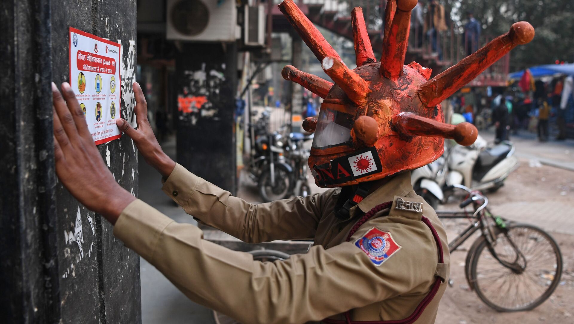 متطوع في الدفاع المدني يرتدي خوذة مستوحاة من فيروس كورونا، يلصق لافتة على الحائط أثناء مشاركته في حملة توعية في أحد الأسواق في نيودلهي، في الهند 25 نوفمبر 2020 - سبوتنيك عربي, 1920, 19.04.2021