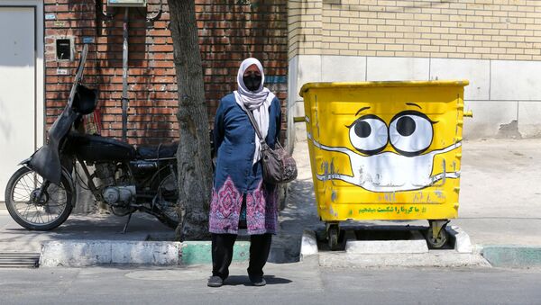 امرأة تقف بجوار سلة القمامة المرسوم عليها كمامة، في إطار حملة لنشر الوعي حول جائحة كورونا، في حي جنوبي بالعاصمة الإيرانية طهران في 18 يوليو 2020. - سبوتنيك عربي