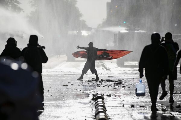متظاهر يتفاعل مع رش خراطيم مياه شرطة مكافحة الشغب، خلال احتجاجات ضد حكومة تشيلي في مدينة سانتياغو، تشيلي، 4 ديسمبر 2020. - سبوتنيك عربي