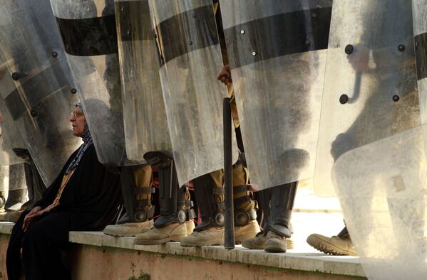 امرأة عراقية أثناء استراحة تحت أقدام شرطة مكافحة الشغب، خلال مظاهرة في ساحة التحرير وسط العاصمة العراقية بغداد، 18 مارس 2011. - سبوتنيك عربي