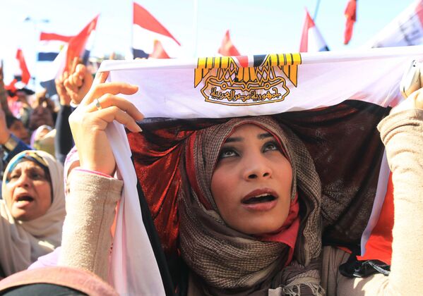 امرأة مصرية تمسك  بالعلم الوطني فوق رأسها أثناء مظاهرة بميدان التحرير في القاهرة ، 27 يناير 2012، قبل انطلاق مسيرة حاشدة للمطالبة بتغيير ديمقراطي، بعد مرور عام على  ثورة البلاد التي أطاحت بالنظام السياسي السابق. - سبوتنيك عربي