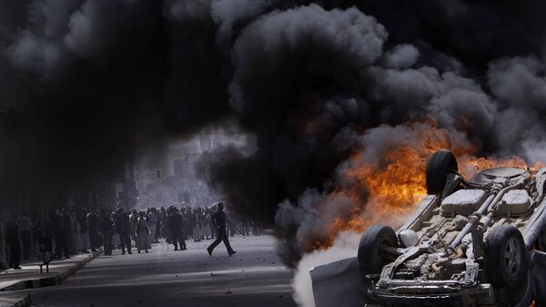 أنصار الحكومة اليمنية وراء دخان يتصاعد من سيارة مشتعلة تابعة لهم، التي أضرم فيها النار متظاهرون مناهضون للحكومة خلال اشتباكات في صنعاء، اليمن 22 فبراير 2011. - سبوتنيك عربي