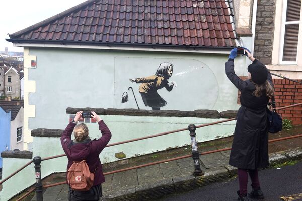 الناس يلتقطون صوراً لعمل فني جديد لبانكسي ظهر على جدار أحد شوارع  توترداون، بعنوان أتشو!!،  في بريستول، بريطانيا 11 ديسمبر 2020. - سبوتنيك عربي