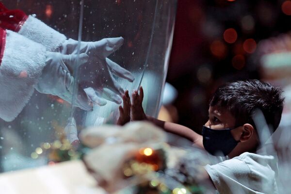 أبيليو دا كروز بينتو، 77 عامًا، يرتدي زي بابا نويل داخل فقاعة بلاستيكية، يحيي طفلًا في مركز تسوق وسط تفشي فيروس كورونا (كوفيد-19) في برازيليا، البرازيل، 15 ديسمبر 2020. - سبوتنيك عربي