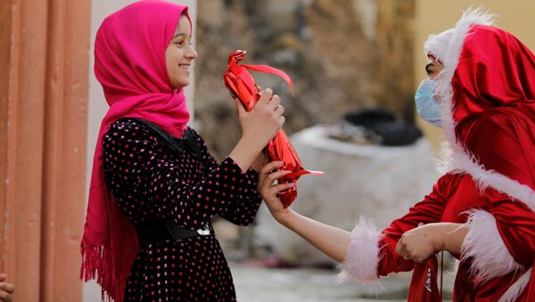 امرأة عراقية ترتدي زي بابا نويل وهي توزع الهدايا على أطفال مدينة الموصل القديمة، العراق 18 ديسمبر 2020 - سبوتنيك عربي