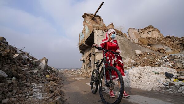 امرأة عراقية ترتدي زي بابا نويل وسط ركام المباني وهي تمشي بدراجتها وسط انتشار مرض فيروس كورونا (كوفيد-19)، في مدينة الموصل القديمة، العراق 18 ديسمبر 2020 - سبوتنيك عربي