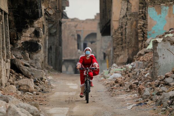امرأة عراقية ترتدي زي بابا نويل وهي تركب دراجتها وسط انتشار مرض فيروس كورونا (كوفيد-19)، وسط ركام مدينة الموصل القديمة، العراق 18 ديسمبر 2020 - سبوتنيك عربي