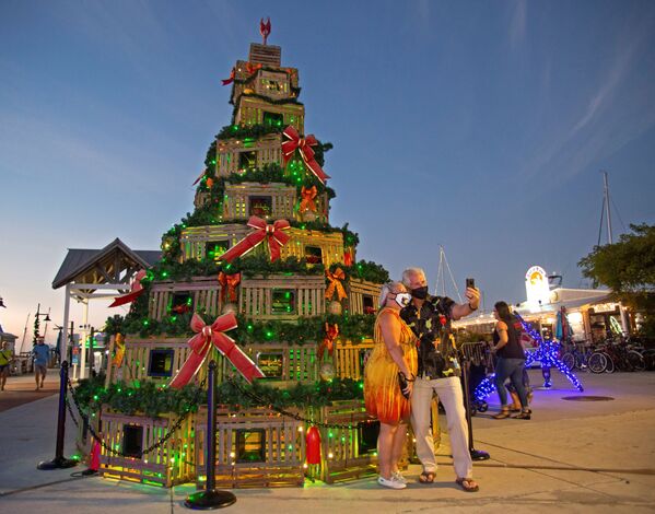 شخصان يقفان لالتقاط صورة سيلفي أمام شجرة عيد الميلاد مصنوعة من صناديق تستعمل في صيد سرطان البحر في كي ويست، فلوريدا، الولايات المتحدة، 13 ديسمبر 2020 - سبوتنيك عربي
