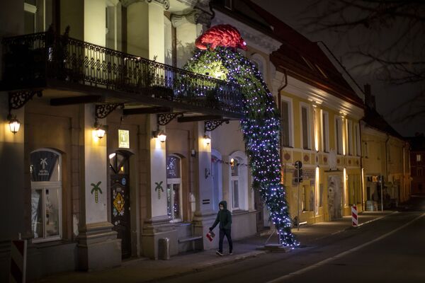 رجل يسير أمام شجرة عيد الميلاد تنحدر من شرفة مبنى في مدينة فيلنيوس، ليتوانيا، 8 ديسمبر 2020 - سبوتنيك عربي