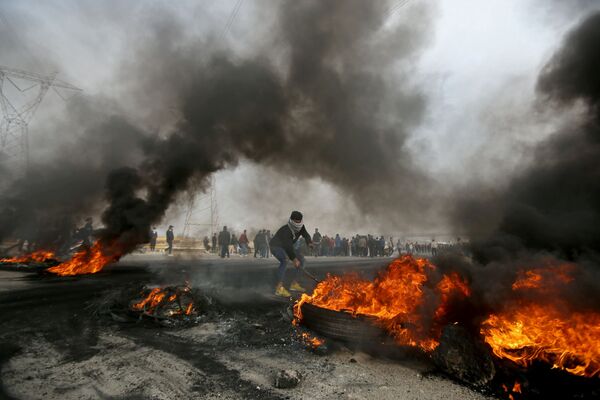 متظاهر عراقي يحرك إطارات محترقة خلال احتجاجات مناهضة للحكومة في البصرة  العراق، 20 ديسمبر 2020 - سبوتنيك عربي