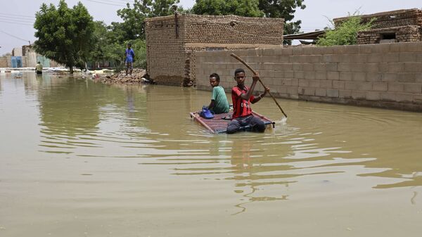أولاد يتنقلون في شارع غمرته المياه على لوح خشبي عبر بلدة السلمانية، على بعد حوالي(35 كم جنوب غرب العاصمة الخرطوم، السودان، 17 سبتمبر 2020 - سبوتنيك عربي