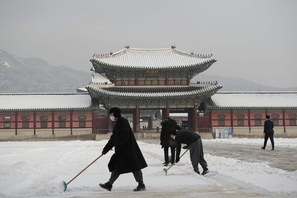 أشخاص يرتدون كمامات كإجراء احترازي ضد فيروس كورونا يقومون بإزالة الثلوج في قصر غيونغبوك، أحد المعالم المعروفة في كوريا الجنوبية، في سيئول، 13 يناير 2021. - سبوتنيك عربي