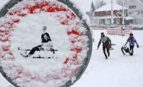 أشخاص يحملون زلاجات يسيرون أمام لافتة مرور مغطاة بالثلوج، مع استمرار انتشار فيروس كورونا (كوفيد-19) في زيورخ، سويسرا، 12 يناير 2021 - سبوتنيك عربي
