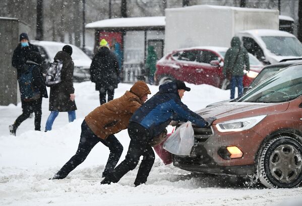رجال يحاولون دفع سيارة عالقة على طريق مغطى بثلوج كثيفة في موسكو، 14 يناير 2021 - سبوتنيك عربي