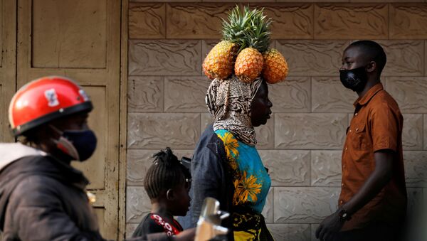 امرأة تسير وهي تحمل فاكهة الأناناس على رأسها في أحد شوارع كمبالا، أوغندا 12 يناير 2021 - سبوتنيك عربي