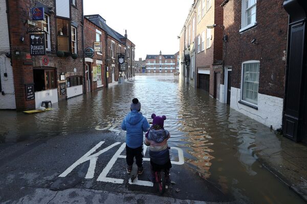 طفلان يقفان في شارع غمرته المياه جزئيًا بعد انفجار ضفاف نهر أوز في يورك، بريطانيا، 22 يناير 2021 - سبوتنيك عربي