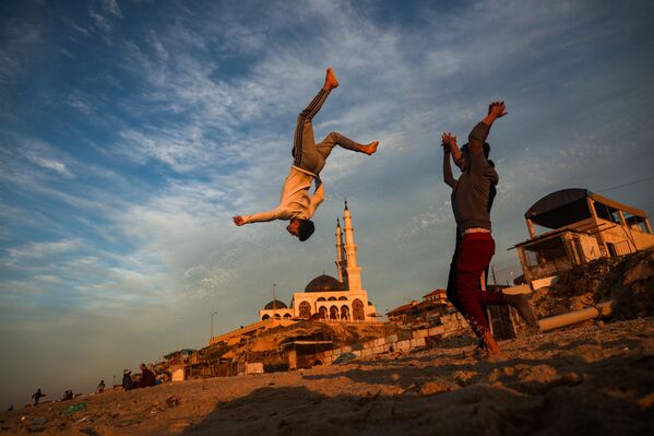 أطفال فلسطينيون يمارسون رياضة الباركور على خلفية مسجد الخالدي على شاطئ في مدينة غزة عند غروب الشمس، قطاع غزة، فلسطين 27 يناير 2021 - سبوتنيك عربي