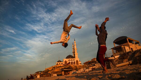 أطفال فلسطينيون يمارسون رياضة الباركور على خلفية مسجد الخالدي على شاطئ في مدينة غزة عند غروب الشمس، قطاع غزة، فلسطين 27 يناير 2021 - سبوتنيك عربي