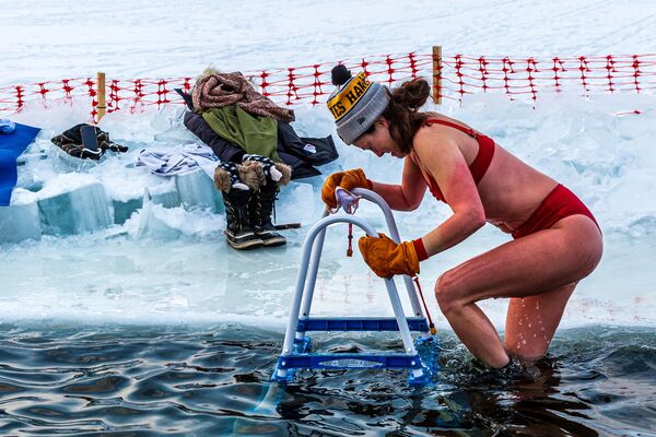 أحد أعضاء مجموعة الغطاسين يخرج من الماء 37.4 درجة فهرنهايت (3 درجات مئوية)، بعد الغطس في موقع مخصص للسباحة الباردة وسط بحيرة هارييت المتجمدة في مدينة مينيابوليس، ولاة مينيسوتا الأمريكية، في 30 يناير 2021 - سبوتنيك عربي