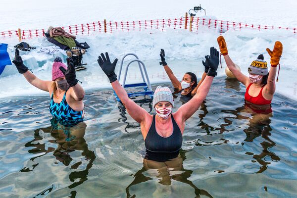 أعضاء مجموعة الغطاسين يسبحون في مياه درجة حرارتها 37.4 درجة فهرنهايت (3 درجات مئوية)، بعد الغطس في موقع مخصص للسباحة الباردة وسط بحيرة هارييت المتجمدة في مدينة مينيابوليس، ولاة مينيسوتا الأمريكية، في 30 يناير 2021 - سبوتنيك عربي
