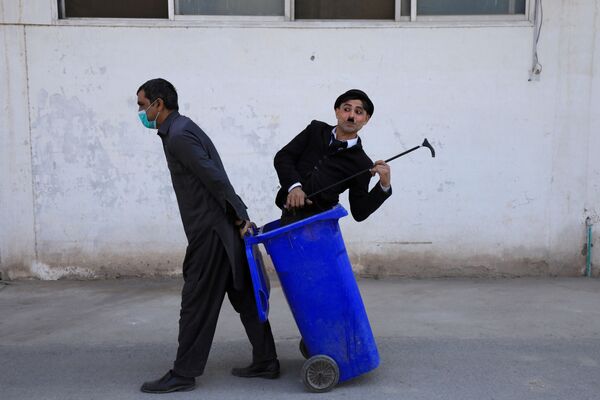 رجل يسحب صندوقًا مع عثمان خان، 29 عامًا، مرتديًا زي تشارلي شابلن خلال عرض ترفيهي في الشارع في بيشاور، باكستان، 28 يناير 2021 - سبوتنيك عربي
