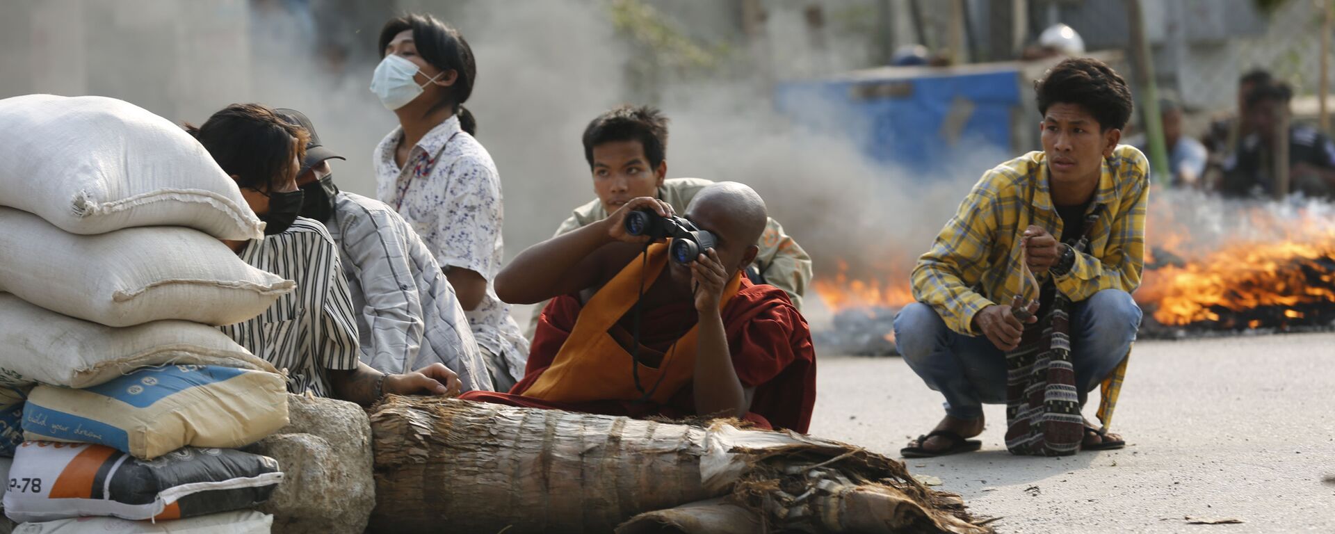 راهب بوذي يستخدم المنظار بينما يجلس مع رجال آخرين خلف حاجز طريق في ماندالاي، مع استمرار الاحتجاجات في ميانمار، 22 مارس 2021 - سبوتنيك عربي, 1920, 28.12.2021