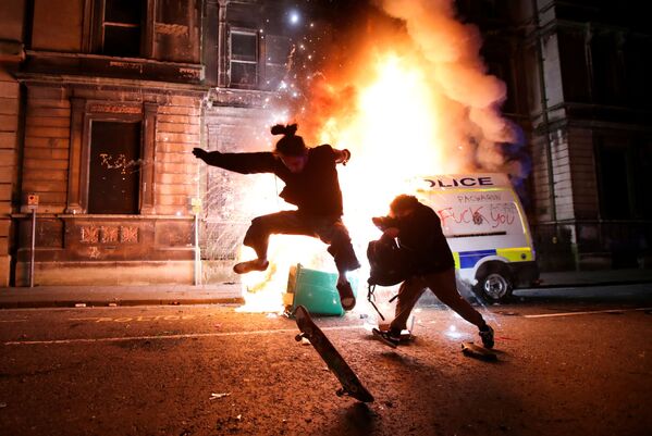 تحذير - قد تحتوي الصورة على مشاهد حساسة: متظاهر يركب لوح تزلج أمام سيارة شرطة محترقة خلال احتجاجات على مشروع قانون جديد للشرطة في بريستول، بريطانيا، 21 مارس 2021 - سبوتنيك عربي
