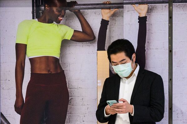 رجل يستخدم هاتفه المحمول على خلفية صور كرتونية على هئية أشخاص في هونغ كونغ، 22 مارس 2021 - سبوتنيك عربي