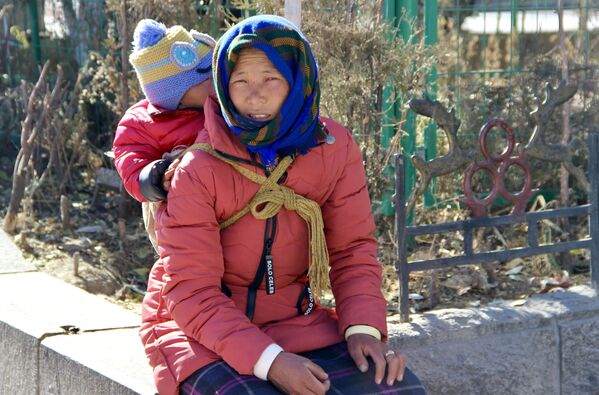 امرأة تحمل صغيرها على ظهرها في مدينة لهاسا (أو لاسا) في التبت. خلال الوباء بأكمله في التبت، حيث تم اكتشاف حالة واحدة فقط أصيبت بـ كوفيد-19 في بداية عام 2020 - سبوتنيك عربي