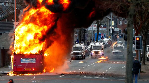 سيارات الشرطة تظهر خلف حافلة مخطوفة تحترق على طريق شانكيلЛ مع استمرار الاحتجاجات في بلفاست، أيرلندا الشمالية، 7 أبريل 2021 - سبوتنيك عربي