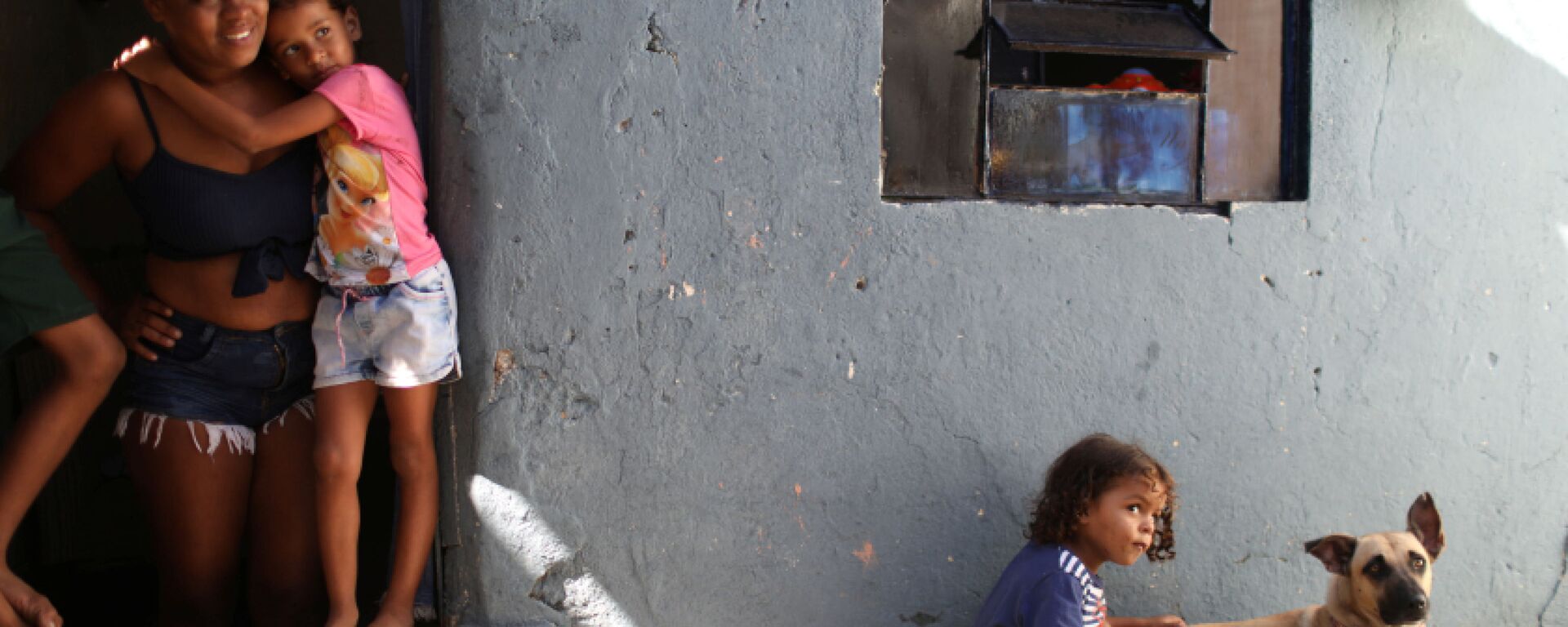 مونيك فيرناندا دي أسيس، 26 عامًا، تقف عند باب منزلها مع ابنتها إستير، حيث يلعب ابنها ميغيل مع كلبهم، بعد تلقي الطعام المتبرع به من مشروع Uma Mao Lava a Outra (يد واحدة تغسل الأخرى) خلال جائحة كورونا (كوفيد-19) في نيلوبوليس، ولاية ريو دي جانيرو، البرازيل، 6 أبريل 2021 - سبوتنيك عربي, 1920, 17.09.2021