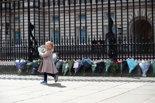 طفلة صغيرة، ماغي (عامين)، تحمل باقة من الورود لوضعها أمام قصر باكنغهام، بعد الإعلان رسميا عن وفاة  الأمير فيليب زوج ملكة بريطانيا إليزابيث الثانية، لندن، بريطانيا 9 أبريل 2021 - سبوتنيك عربي