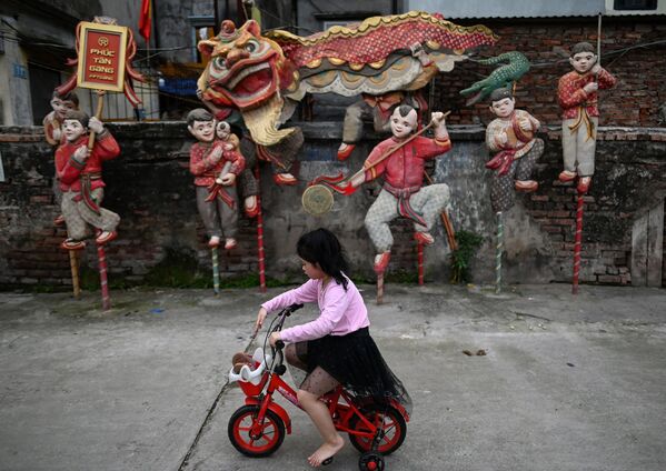 فتاة صغيرة تركب دراجتها على خلفية لوحة مركبة بعنوان رقصة الأسد للفنان نجوين شوان لام، في مساحة فوك تان للفنون العامة في هانوي، فيتنام 14 أبريل 2021 - سبوتنيك عربي