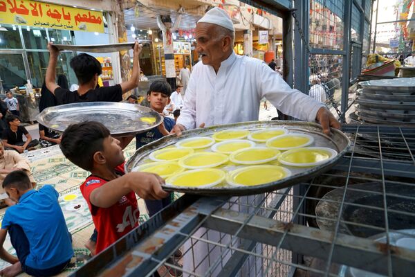 العراقيون يحملون الأطباق بينما يتجمع الناس لتناول الإفطار خلال إفطار جماعي مجاني في أحد الشوارع بمناسبة شهر رمضان في النجف، العراق، 18 أبريل 2021 - سبوتنيك عربي