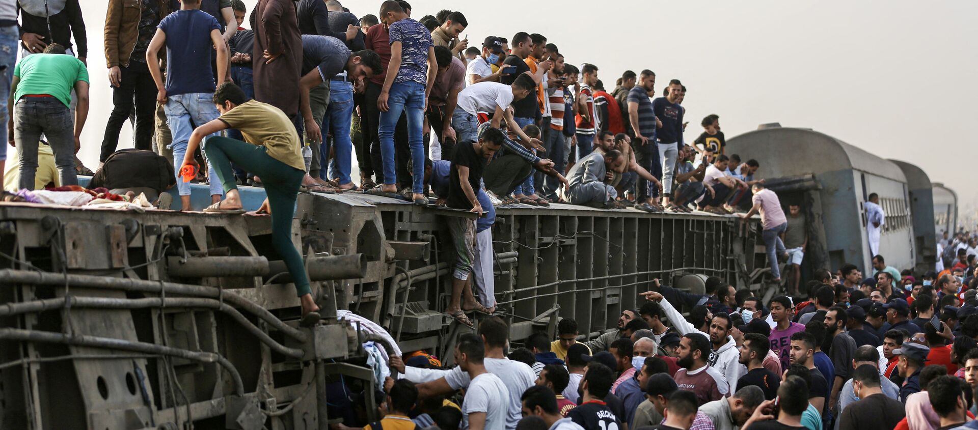 تجمع الناس حول قطار في موقع حادث سكة حديد في مدينة طوخ في محافظة القليوبية، وسط دلتا النيل في مصر، 18 أبريل 2021 - سبوتنيك عربي, 1920, 26.04.2021