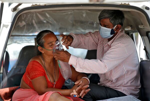 كارثة إنسانية كبرى - تسجيل أرقام قياسية لحالات الإصابة بمرض كوفيد-19، زوج يهتم بتعديل قناع الأكسجين لزوجته داخل سيارة للدخول إلى مشفى لتلقي العلاج في أحمدآباد، الهند 28 أبريل 2021 - سبوتنيك عربي