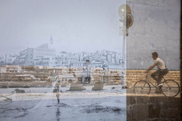 صورة رجل يركب دراجة ينعكس على زجاج لصورة قديمة لمدينة يافا معروضة على أحد نوافذ منطقة يافا في تل أبيب، إسرائيل 21 أبري 2021 - سبوتنيك عربي