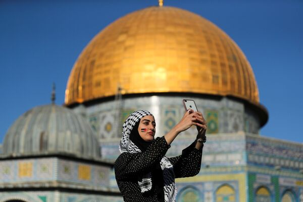 شابة فلسطينية تلتقط صورة سيلفي، بعد صلاة عيد الفطر، على خلفية مسجد قبة الصخرة في باحة مسجد الأقصى، القدس، فلسطين 13 مايو 2021 - سبوتنيك عربي