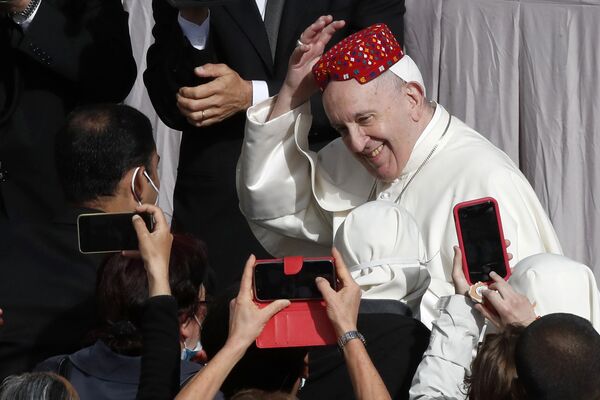 بابا الفاتيكان فرانسيس يبتسم بعد أن وضع أحد الحضور قبعة على رأسه في ساحة القديس داماسو بالفاتيكان أمام جمهوره الأسبوعي، 12 مايو 2021. - سبوتنيك عربي